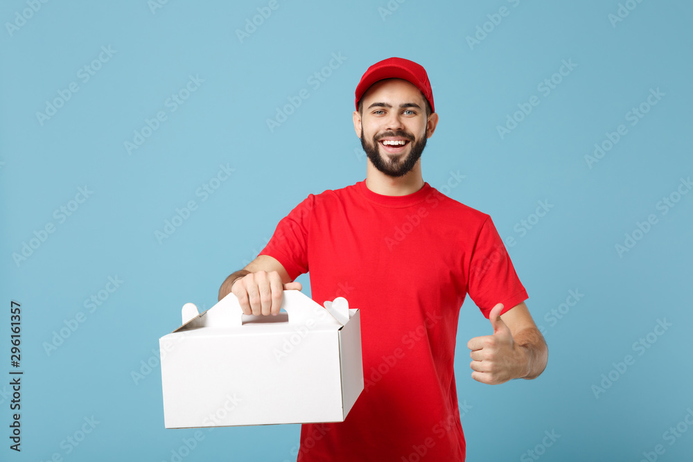 Delivery man in red uniform isolated on blue background, studio portrait. Male employee in cap t-shirt print courier hold cake dessert in unmarked cardboard box. Service concept. Mock up copy space.