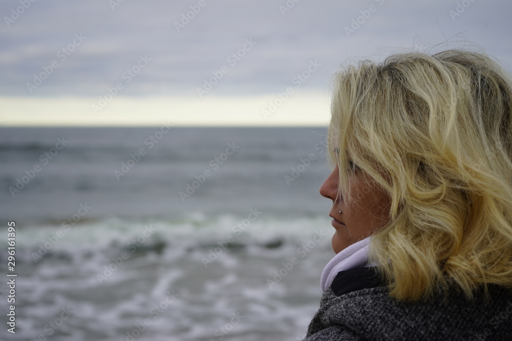 A girl looks into the distance against the backdrop of a cold sea. Blond hair in the wind. Hair and sea breeze. close-up. A girl looks into the distance against the backdrop of a cold sea. Blond hair in the wind. Hair and sea breeze. close-up.