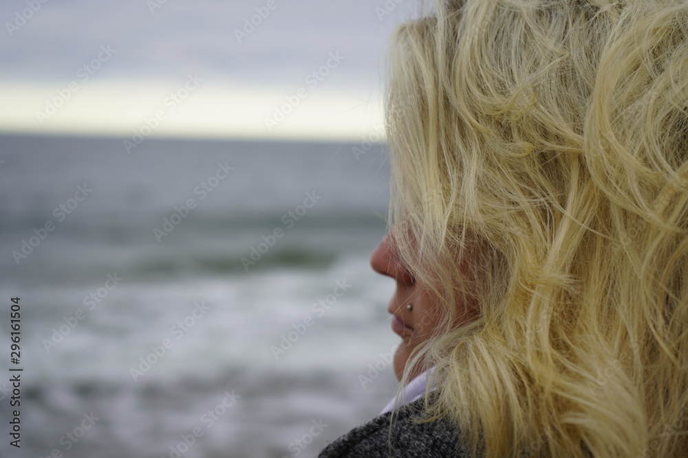 A girl looks into the distance against the backdrop of a cold sea. Blond hair in the wind. Hair and sea breeze. close-up. A girl looks into the distance against the backdrop of a cold sea. Blond hair in the wind. Hair and sea breeze. close-up.