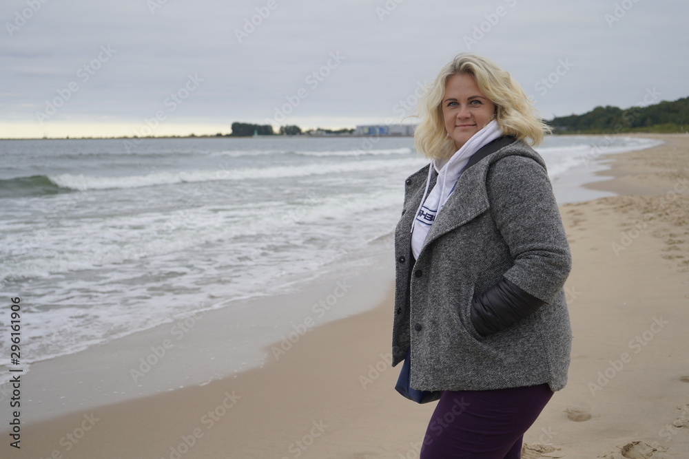 The girl turns and looks into the camera lens on the background of the cold sea. Blond hair in the wind. Hair and sea breeze. close-up The girl turns and looks into the camera lens on the background of the cold sea. Blond hair in the wind. Hair and sea breeze. close-up