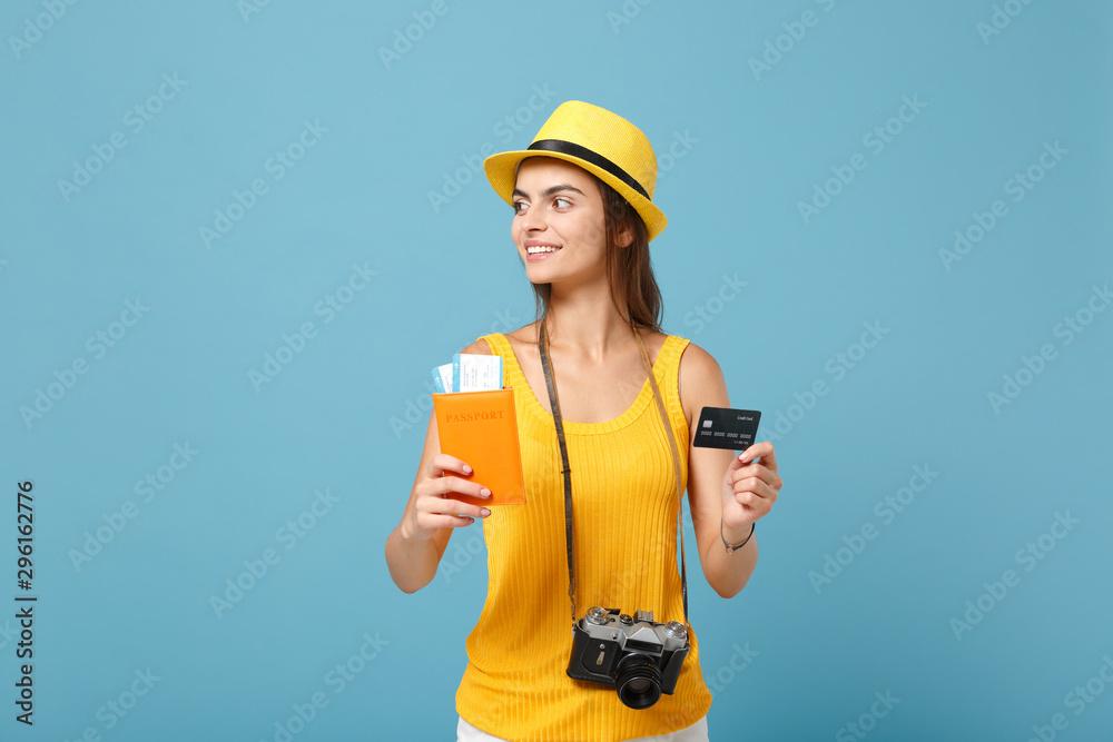 Traveler tourist woman in yellow clothes hat hold tickets credit card camera isolated on blue background. Female passenger traveling abroad to travel on weekends getaway. Air flight journey concept.