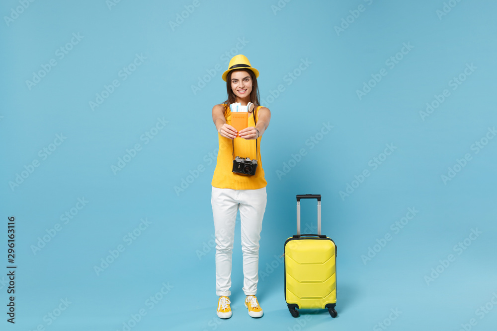 Traveler tourist woman in yellow summer casual clothes hat hold tickets bag camera isolated on blue background. Female passenger traveling abroad travel on weekends getaway. Air flight journey concept