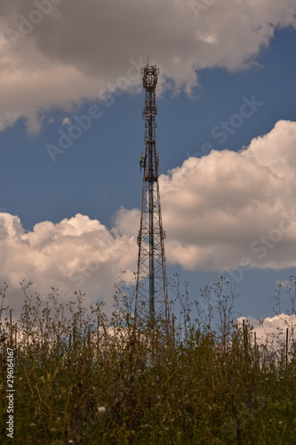 vista de uma torre de transmissão com plantas e céu azul com nuvens