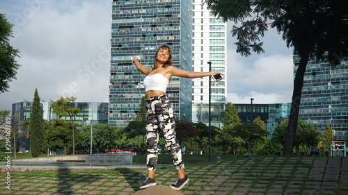 young woman standing on the street with open arms while laughing against city buildings