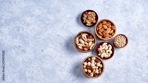 pecans, hazelnuts, almonds, pine nuts, Brazil nut, cashews in wooden bowls on blue background, top view, flat lay