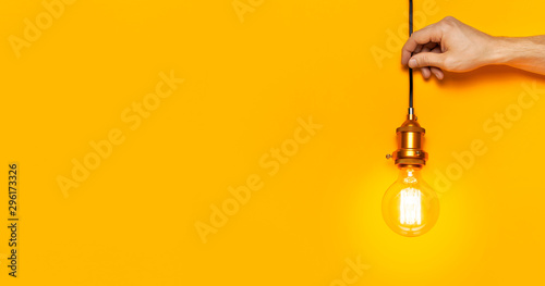 Vintage fashionable edison lamp in male hands on bright yellow background. Top view flat lay copy space. Creative idea concept, designer lamp, modern interior item. Lighting, electricity