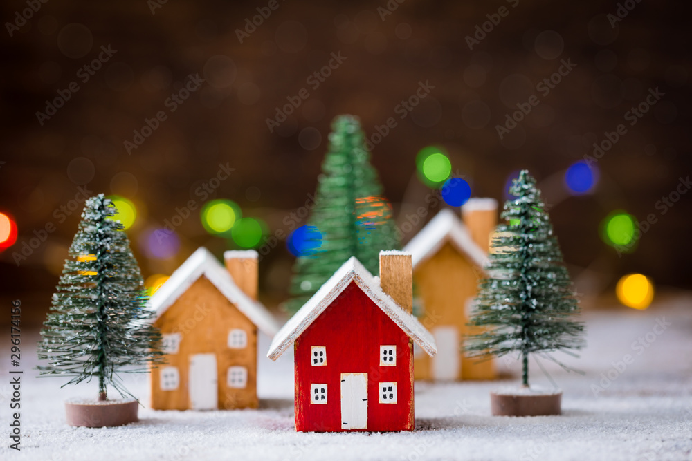 Miniature wooden houses on the snow over blurred Christmas decoration background, toned