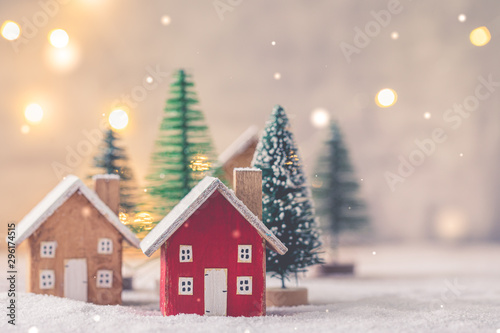 Miniature wooden houses on the snow over blurred Christmas decoration background, toned, postcard concept