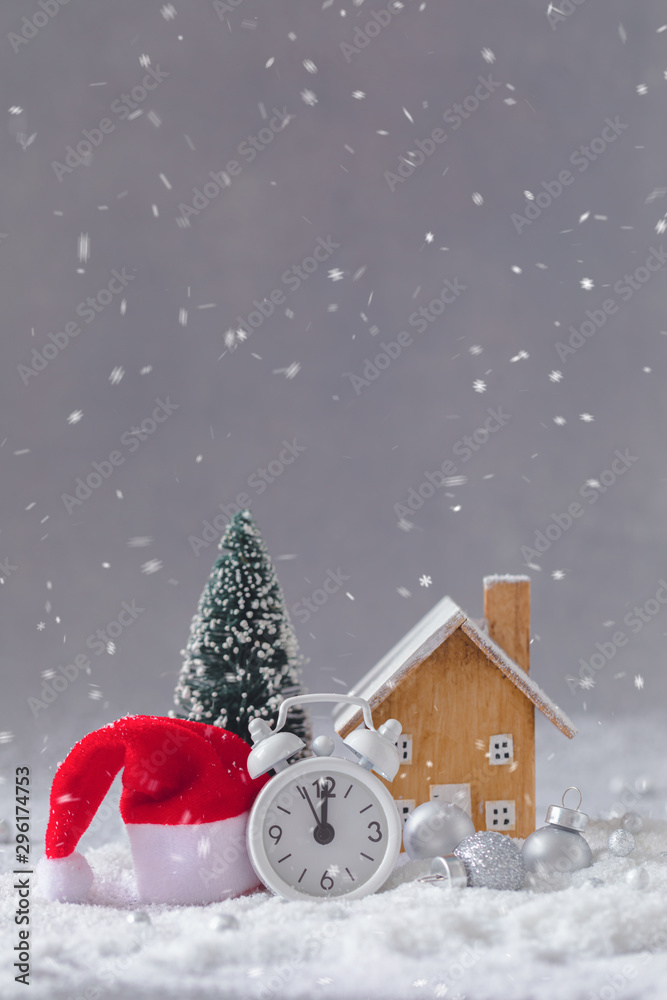 Naklejka premium Christmas alarm clock, Santa Claus hat, small wooden toy cottage and fir-tree with balls, New Year postcard concept