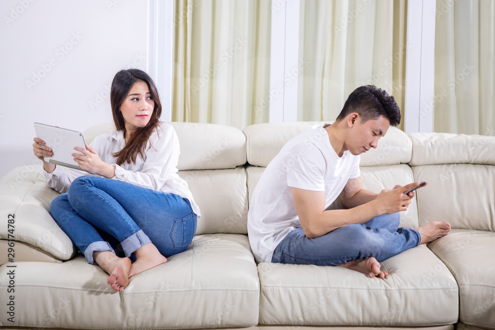 Asian couple sitting back to back on the couch Asian couple sitting back to back on the couch