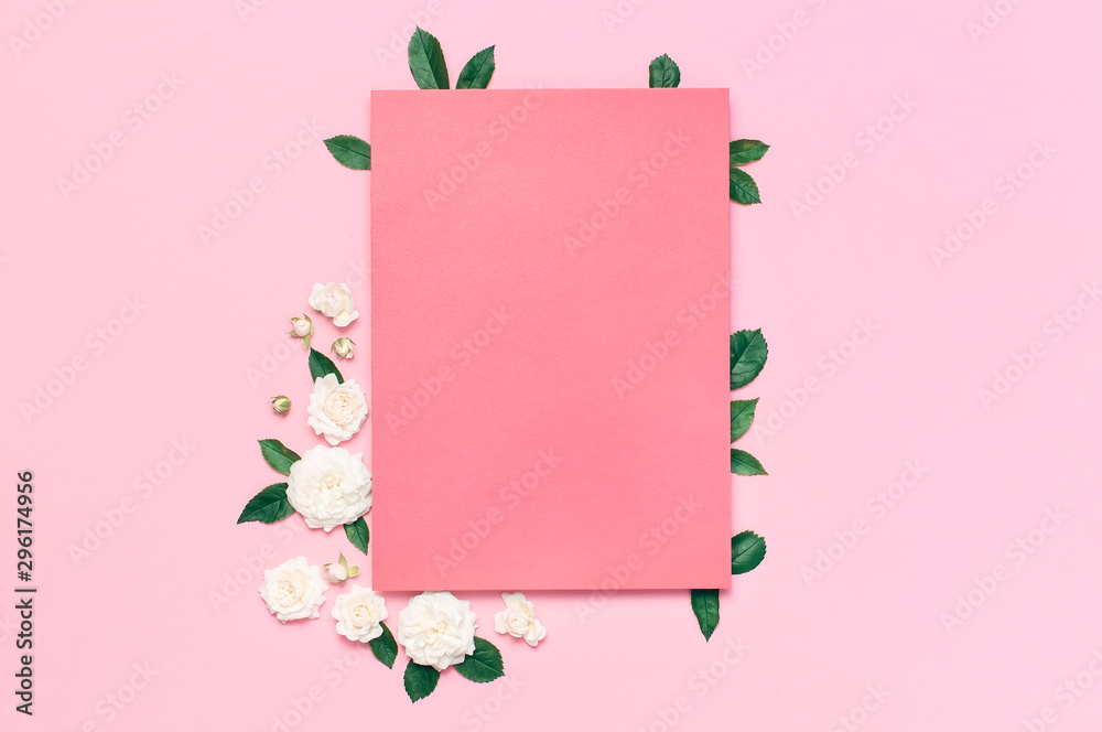 Flowers composition. Pink blank paper, white fresh roses and green leaves on gentle pink background. Flat lay, top view, copy space. Flower card, greeting, holiday mockup. Valentine's Day background