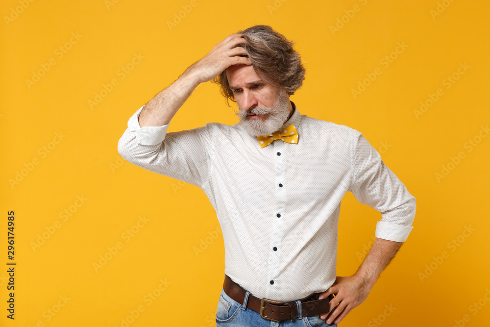 Preoccupied elderly gray-haired mustache bearded man in white shirt bow tie posing isolated on yellow orange background in studio. People lifestyle concept. Mock up copy space. Putting hand on head. Preoccupied elderly gray-haired mustache bearded man in white shirt bow tie posing isolated on yellow orange background in studio. People lifestyle concept. Mock up copy space. Putting hand on head.