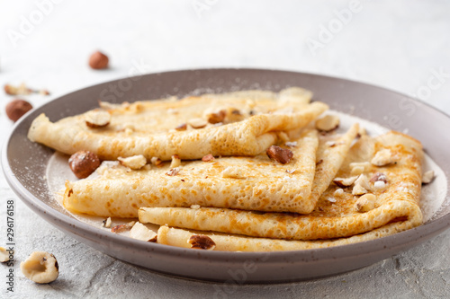 Crepes with hazelnuts and powdered sugar on plate on white concrete background. Selective focus.