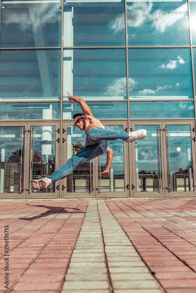 Jumping dancer, acrobat actor break dance, hip hop. In summer city, background is glass windows clouds. Active youth lifestyle, young male dancer, fitness movement workout breakdancer. Jumping dancer, acrobat actor break dance, hip hop. In summer city, background is glass windows clouds. Active youth lifestyle, young male dancer, fitness movement workout breakdancer.