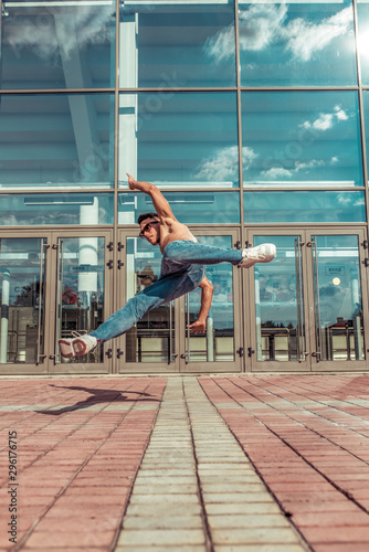 Jumping dancer, acrobat actor break dance, hip hop. In summer city, background is glass windows clouds. Active youth lifestyle, young male dancer, fitness movement workout breakdancer.