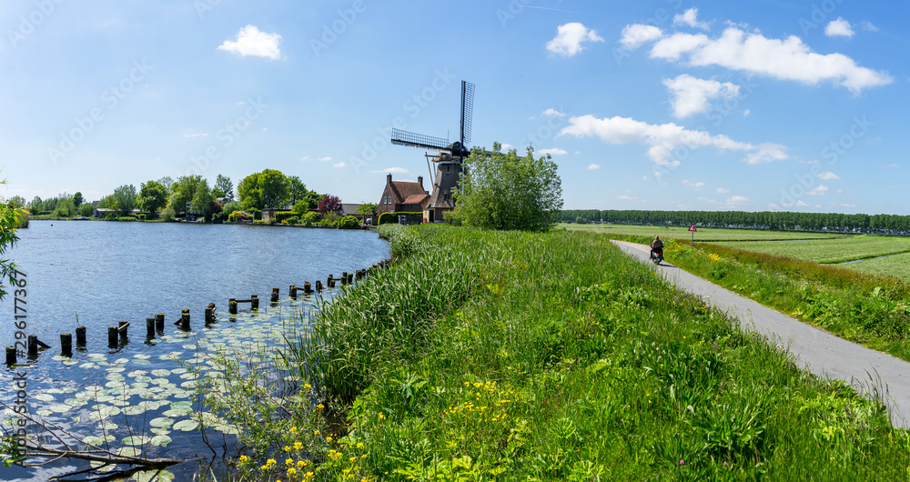 Moped passing by windmill on the river Vecht dike