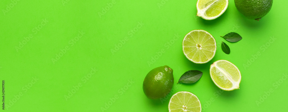 Fresh juicy lime and green leaves on bright green background. Top view flat lay copy space. Creative food background, tropical fruit, vitamin C, citrus. Composition with whole and slices of lime