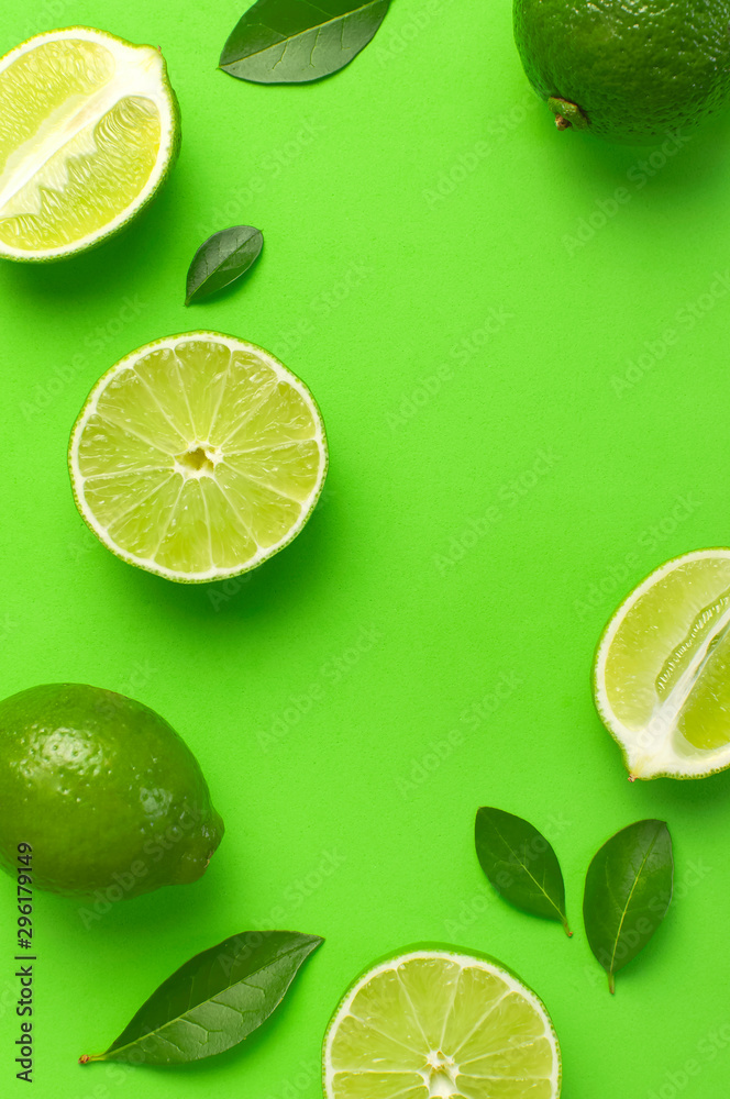 Fresh juicy lime and green leaves on bright green background. Top view flat lay copy space. Creative food background, tropical fruit, vitamin C, citrus. Composition with whole and slices of lime