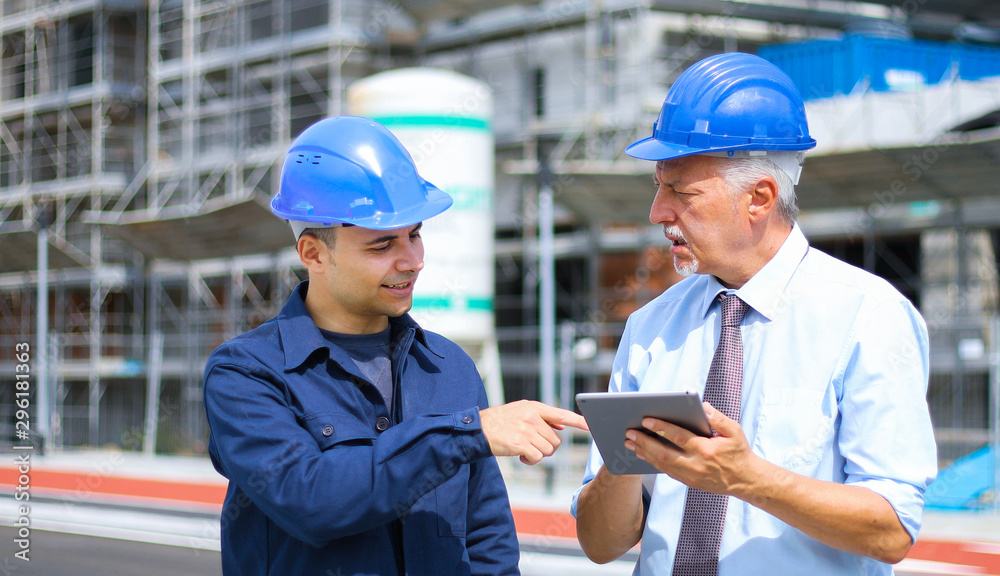 Two architect developers reviewing building plans at construction site using a tablet Two architect developers reviewing building plans at construction site using a tablet