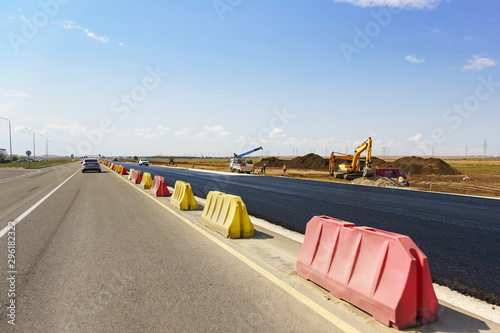 Construction of a new modern highway Tavrida in the Crimea. Fresh black asphalt is separated by yellow and red road barriers. Sunny day