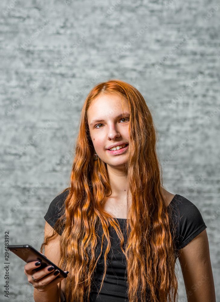 portrait of young teenager redhead girl with long hair with smartphone on gray wall background portrait of young teenager redhead girl with long hair with smartphone on gray wall background
