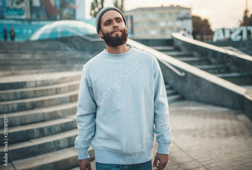 Fotografija City portrait of handsome hipster guy with beard wearing gray blank hoodie or hoody and hat with space for your logo or design