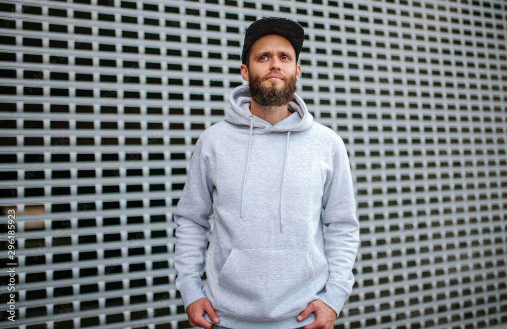 City portrait of handsome hipster guy with beard wearing gray blank hoodie or sweatshirt and hat with space for your logo or design. Mockup for print City portrait of handsome hipster guy with beard wearing gray blank hoodie or sweatshirt and hat with space for your logo or design. Mockup for print