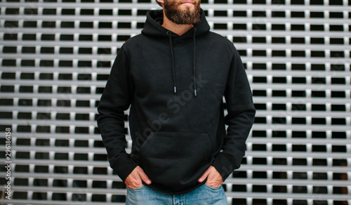 City portrait of handsome hipster guy with beard wearing black blank hoodie or sweatshirt and hat with space for your logo or design. Mockup for print photo