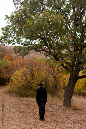 The back view of a girl walking down with her head bowed in black sweater and beret stands in the autumn in the park