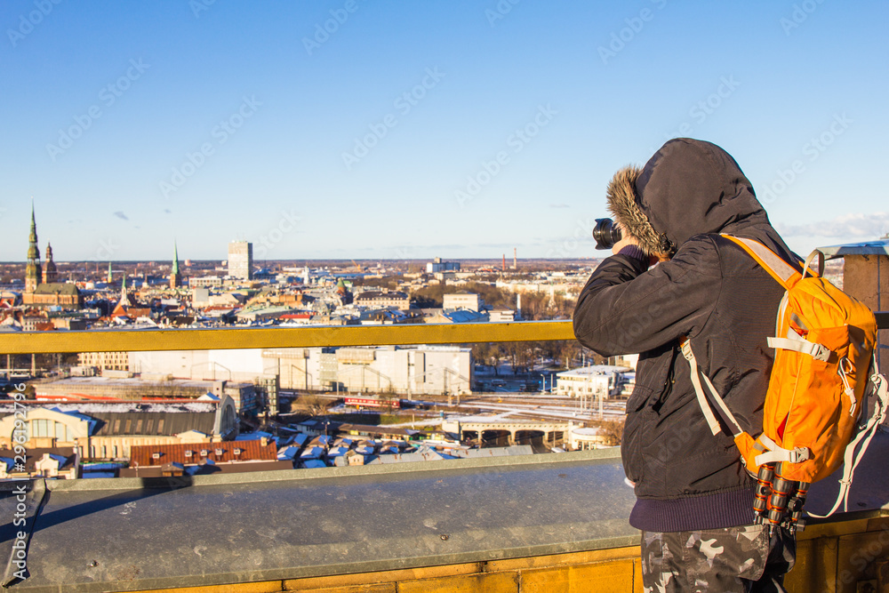 Photographer with big bag taking picture landmark the ancient european city from a high view point. Latvian Academy of Sciences. Sunny winter day. Riga, Europe, Baltic, Latvia. Travel photos concept