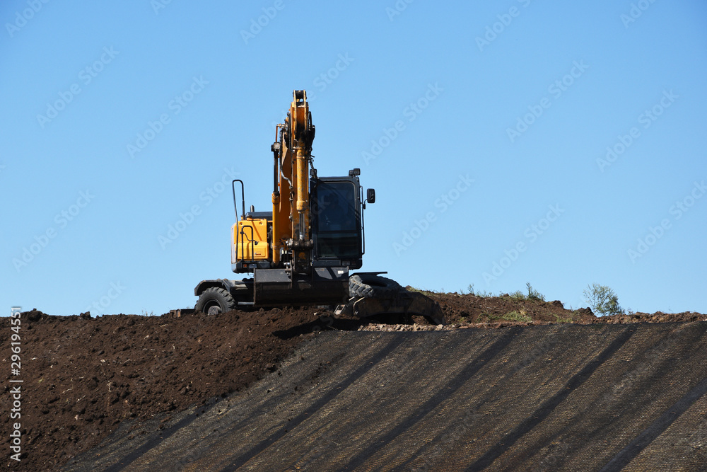 A yellow excavator digs earth with a bucket, repairs the road and the surrounding area. A yellow excavator digs earth with a bucket, repairs the road and the surrounding area.