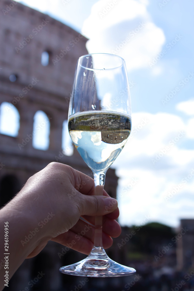 Woman's hand takes glass of champagne on the background of the Colosseum. Christmas concept. Christmas and New Year in Italy