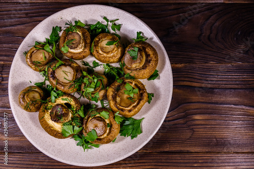 Plate with baked champignons, dill and parsley on a wooden table. Top view
