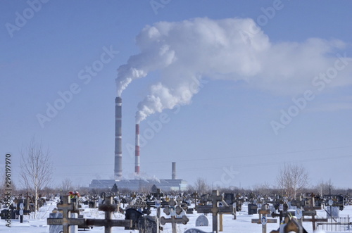 winter landscape, cemetery and grove with smoke from a factory chimney on the horizon, pollution