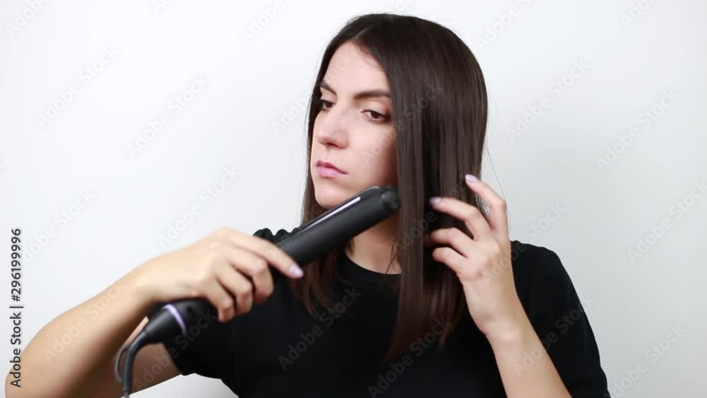 Dark-haired girl straightens her hair on a curling iron. White background.Girl with dark brown hair. Dark-haired girl straightens her hair on a curling iron. White background.Girl with dark brown hair.