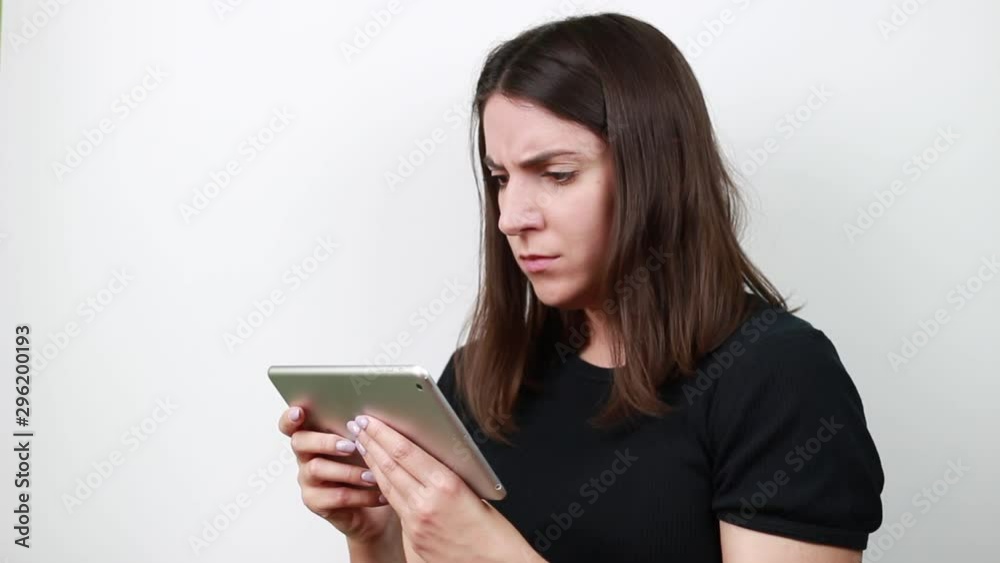 Dark-haired woman looks at tablet and misses. Frustrated facial expression. White background.Girl with dark brown hair. Dark-haired woman looks at tablet and misses. Frustrated facial expression. White background.Girl with dark brown hair.