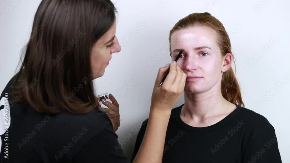 Brown-haired woman doing red-haired girl makeup. Application of a cream.