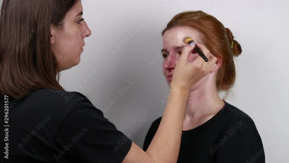 Brown-haired woman doing red-haired girl makeup. Application of a cream. Brown-haired woman doing red-haired girl makeup. Application of a cream.