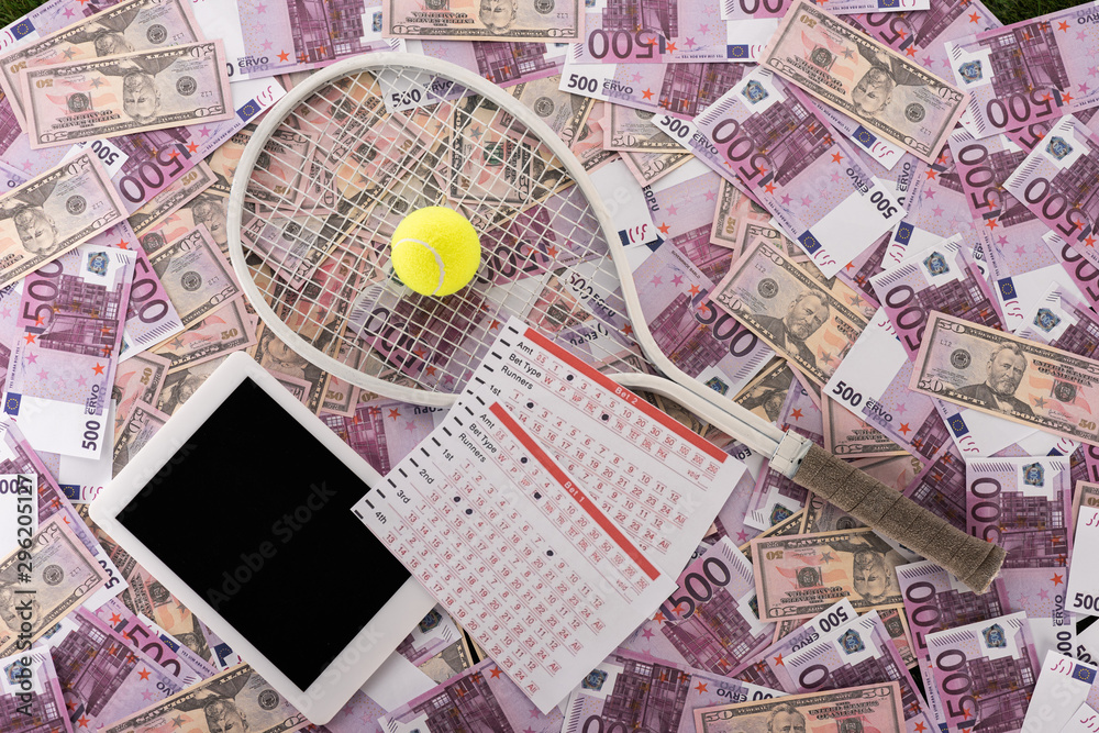 top view of digital tablet, betting lists, tennis racket and ball on euro and dollar banknotes, sports betting concept