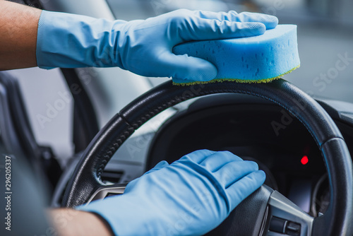 cropped view of car cleaner in rubber gloves wiping steering wheel with sponge