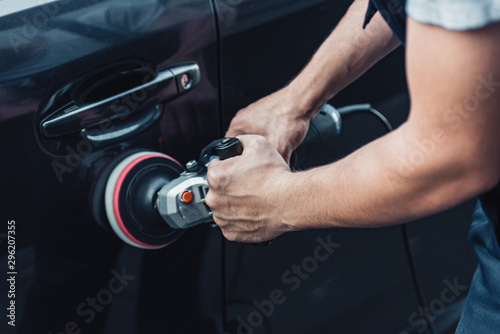 partial view of car cleaner polishing black car door with buffer machine