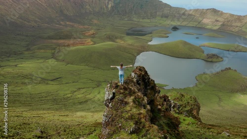 Girl with wide open arms on a rock above grate and beautiful green caldera of inactive volcano. Aerial of Corvo, Azores photo