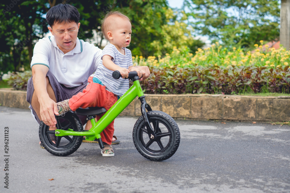 Young father spend time with Cute little Asian 18 months / 1 year old toddler boy child, Dad and son play and have fun with balance bike (run bike), Dad teach son to ride bike, father's day concept Young father spend time with Cute little Asian 18 months / 1 year old toddler boy child, Dad and son play and have fun with balance bike (run bike), Dad teach son to ride bike, father's day concept