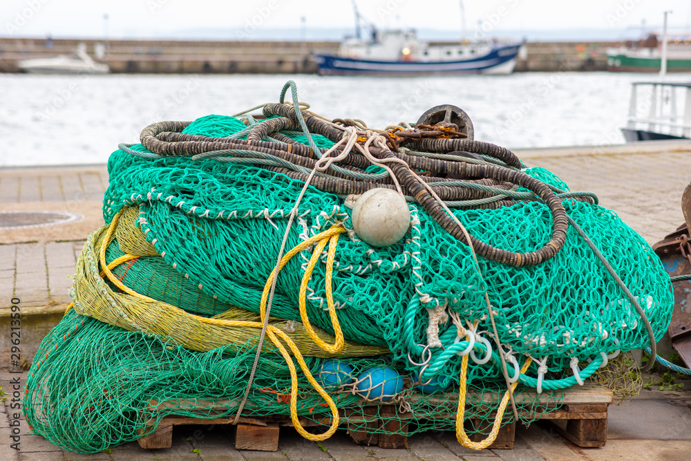 A fishing net with balls and ropes on a pallet of wood on the quay wall in the harbor of the German city Sassnitz. In the background a fishing boat out of focus with beautiful bokeh.