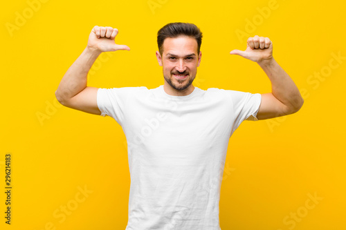 young handsome man feeling proud, arrogant and confident, looking satisfied and successful, pointing to self against orange wall