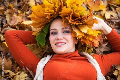 Young beautiful woman with a wreath of maple leaves posing in autumn park