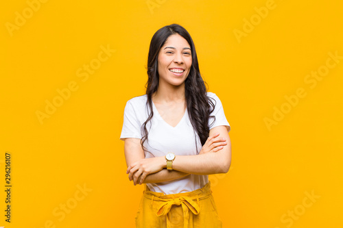 young pretty latin woman looking like a happy, proud and satisfied achiever smiling with arms crossed against orange wall photo