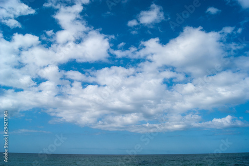 White fluffy clouds, like blond-haired horses, fly across the sky above a blue strip of the sea