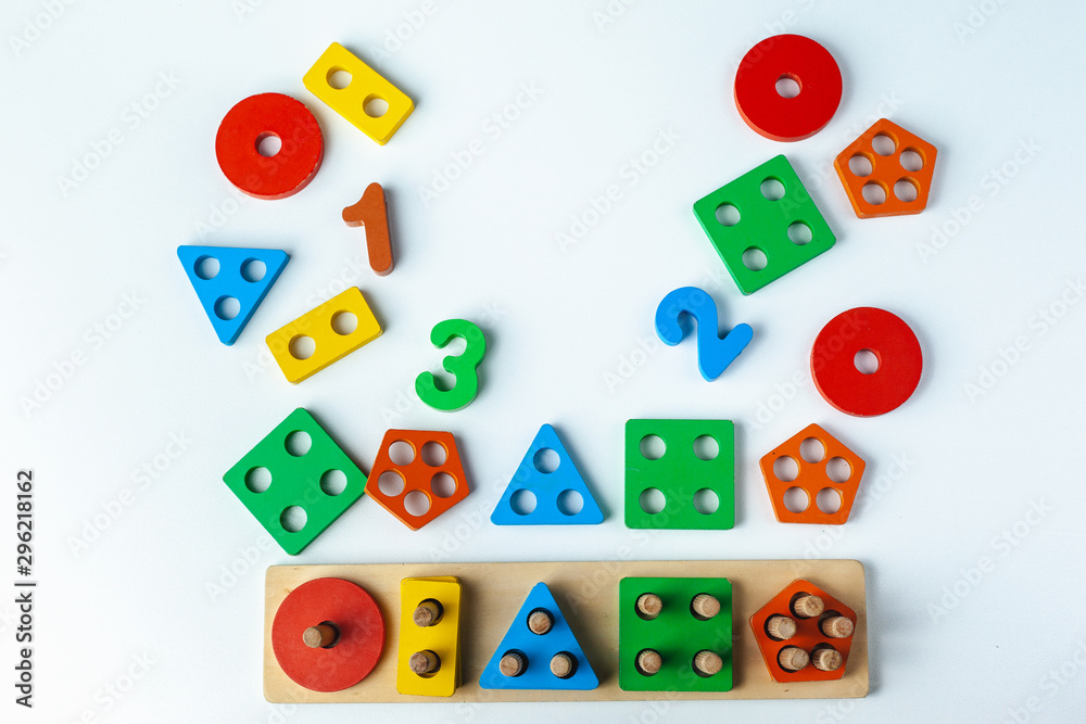 Wooden toy for learning numbers and shapes. Numbers from one to five. Multi-colored figures circle, square, rectangle, triangle, five gon. Child plays Montessori game. Kid collects wooden toy sorter. 