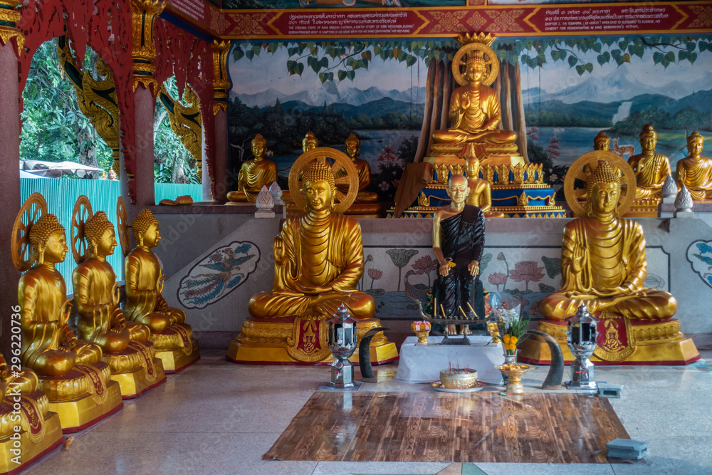 Bang Saen, Thailand - March 16, 2019: Wang Saensuk Buddhist Monastery. Golden statues in main open Prayer Hall with in center statue of founder of abbey. Green foliage outside.